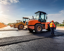 Three construction vehicles line up on a newly paved asphalt road 